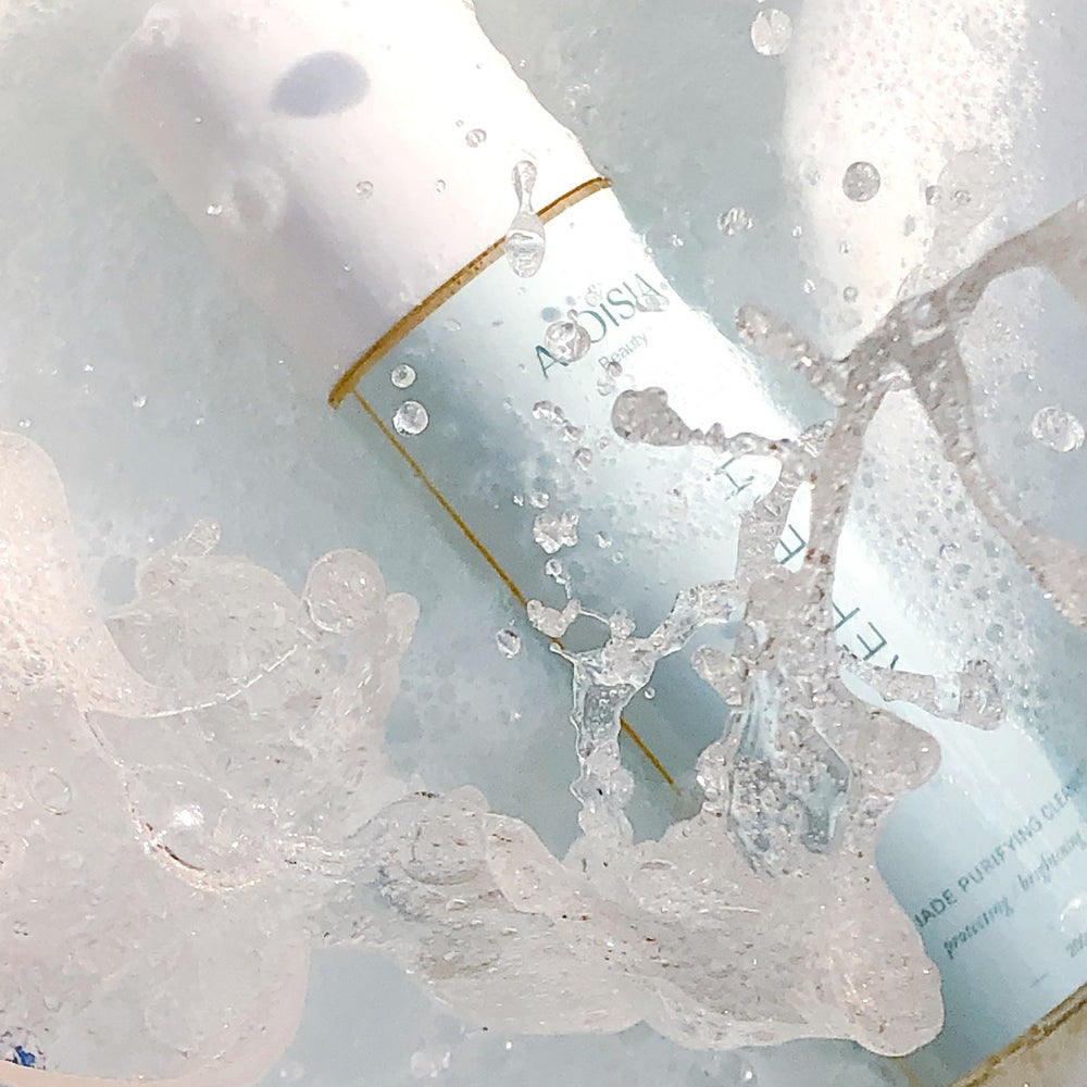 Close-up of REFRESH Jade Purifying Cleanser partially submerged in water, showing bubbles and water droplets.
