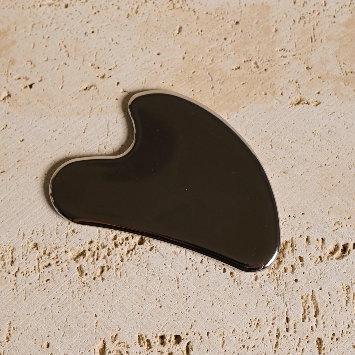 Stainless steel gua sha tool on a stone surface